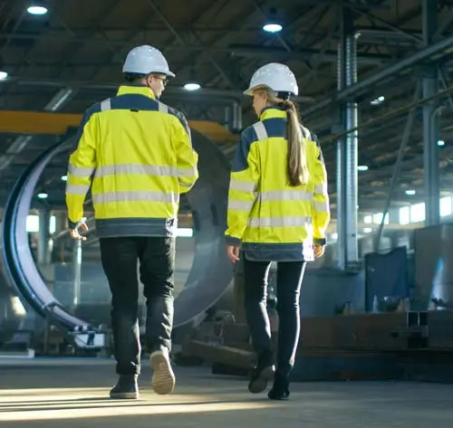 Facility Management Stuttgart – Technische Betreuung in der Industrie Zwei Mitarbeitende mit Schutzhelmen und Warnwesten in einer Industriehalle – Facility Management Stuttgart im technischen Umfeld mit Fokus auf Instandhaltung und Sicherheit.